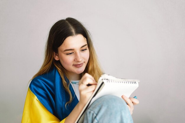 A ukrainian teenage girl is wrapped in the ukrainian flag and\
is drawing or doing homework in the bedroom a teenager studies at\
home the concept of studies during the war in ukraine