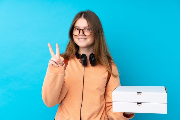 Ukrainian teenager girl holding pizzas over isolated blue wall smiling and showing victory sign