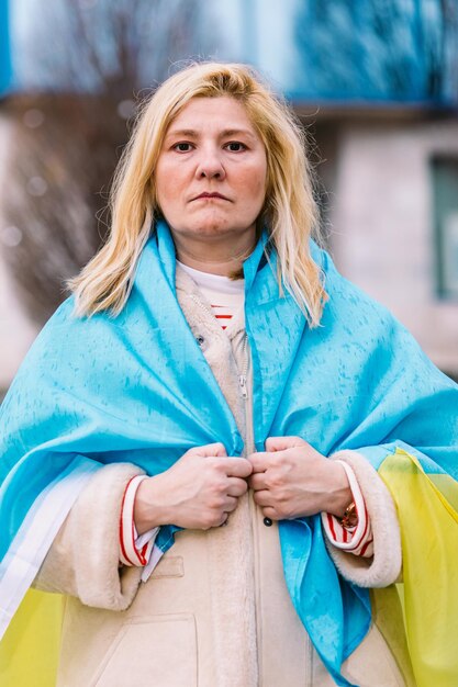 Foto donna ucraina con capelli biondi e un gesto serio con una bandiera ucraina blu e gialla in strada per protestare contro la guerra ucrainarussia