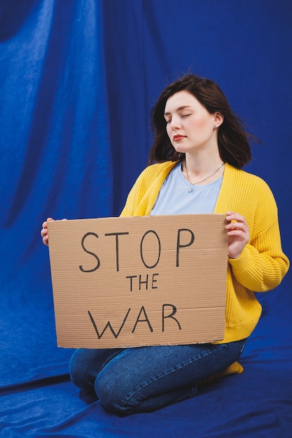 A Ukrainian woman in a yellow sweater and blue jeans with a stop the war sign Ukrainian girl suffered from the war No war
