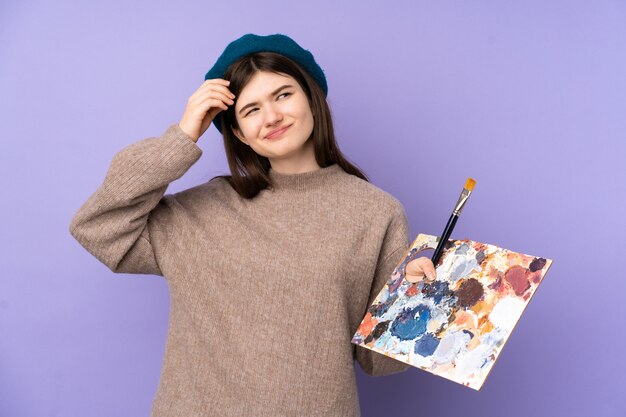 Ukrainian Young artist girl holding a palette over isolated purple wall having doubts and with confuse face expression