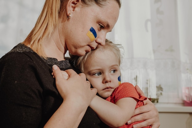 Ukrainian young mother with daughter with flag on the face with fear suffering and praying peace dur...