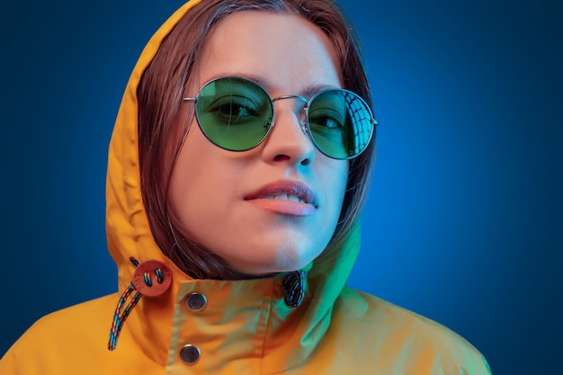 Фото Украинская молодая женщина в желтом плаще и круглых цветных очках на синем фоне