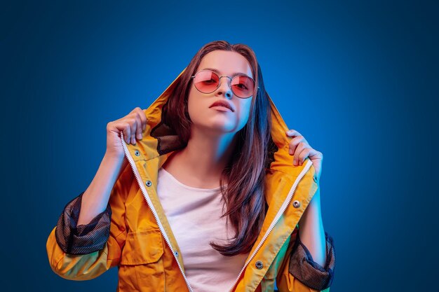 Ukrainian young woman in yellow raincoat and round olor glasses in blue background