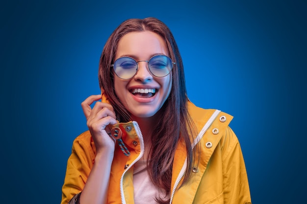 Ukrainian young woman in yellow raincoat and round olor glasses in blue background