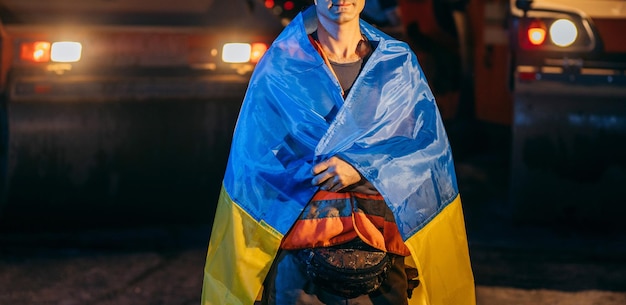 Ukrainian young worker with ukrainian flag on his shoulders on
the background of road works