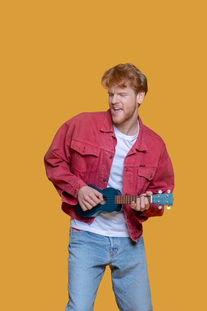 Ukulele. Man in red jacket playing the ukulele