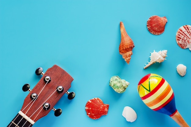 Ukulele, maracas and sea shells on blue background