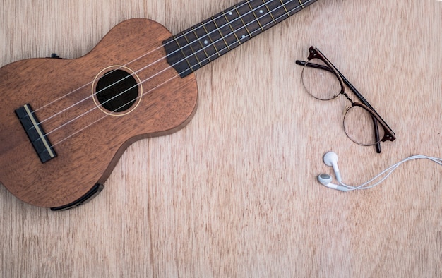 Foto ukulele con gli occhiali e la cuffia su fondo di legno.