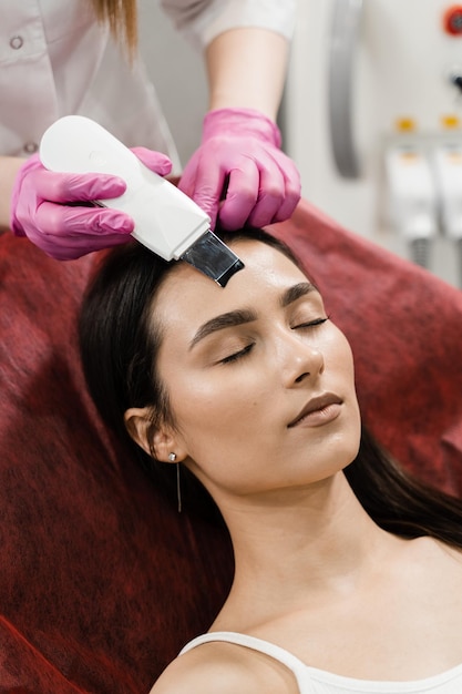 Ultrasone gezichtspeeling met scrubber close-up Schoonheidsspecialist doet ultrasone peeling huid met huidscrubber voor meisjespatiënt in cosmetologiekliniek