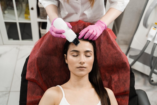 Ultrasone gezichtspeeling met scrubber Schoonheidsspecialist doet ultrasone peeling huid met huidscrubber voor meisjespatiënt in cosmetologiekliniek