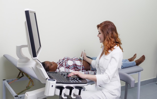 Photo ultrasound procedure the girl doctor conducts an ultrasound examination of the abdominal cavity of an africanamerican patient