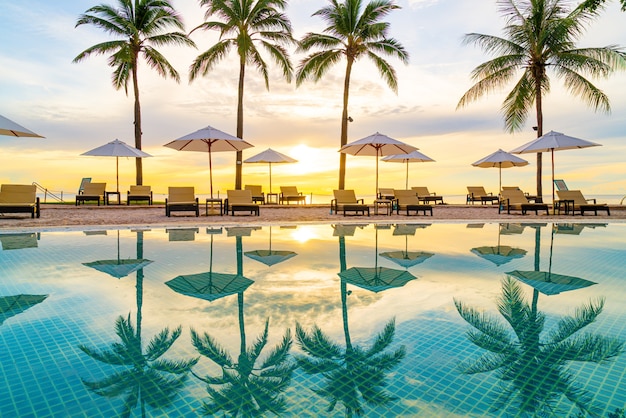 Umbrella and chair around swimming pool in hotel resort with sunrise in morning - holiday and vacation concept