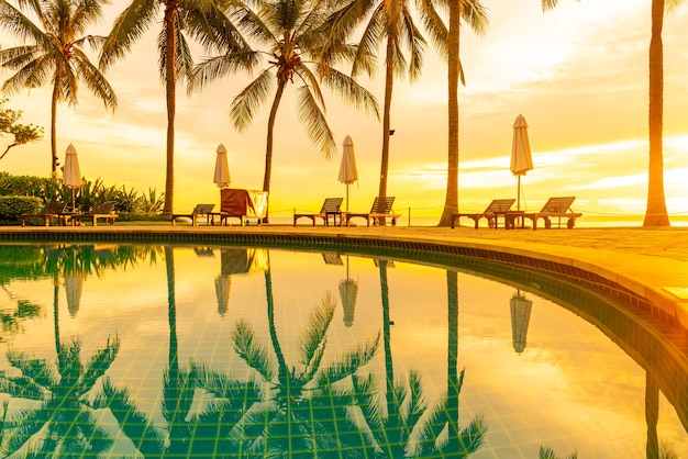 Umbrella and chair around swimming pool in hotel resort with\
sunrise in morning. holiday and vacation concept