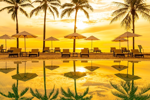 레저 여행 및 휴가를위한 리조트 호텔 수영장 주변의 우산과 의자 일몰 또는 일출 시간에 가까운 바다 바다 해변