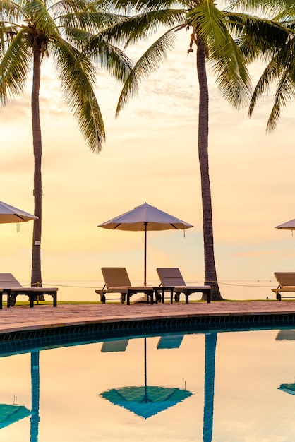 日没や日の出時にレジャー旅行や休暇に近い海のビーチの休暇のためのリゾートホテルのスイミングプールの周りの傘と椅子