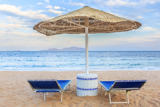 Umbrella and two empty deckchairs on the shore sand beach