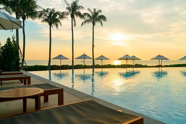 umbrella with bed pool around swimming pool with ocean sea background at sunset or sunrise time - holiday and vacation concept