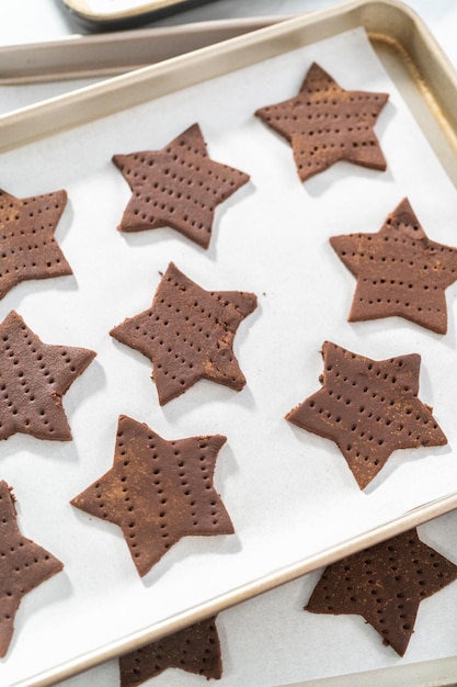 Unbaked star-shaped chocolate graham crackers on the baking sheet lined with parchment paper.