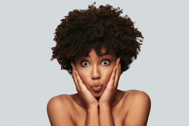 Unbelievable! Surprised young African woman looking at camera and making a face while standing against grey background