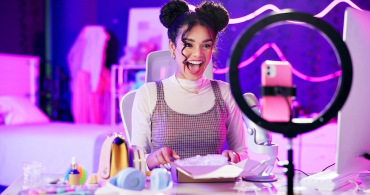 Foto unboxing live stream en gelukkige influencer vrouw met microfoon neon licht en make-up in huis studio content creator schoonheid streamer of opgewonden meisje in online video voor huidverzorgingsproduct review