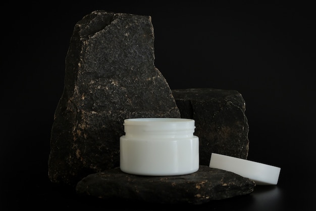 Unbranded natural cosmetic cream packaging standing on stone podium. Cream presentation on the black background. Mockup. Trending concept in natural materials. Natural cosmetic, skincare.