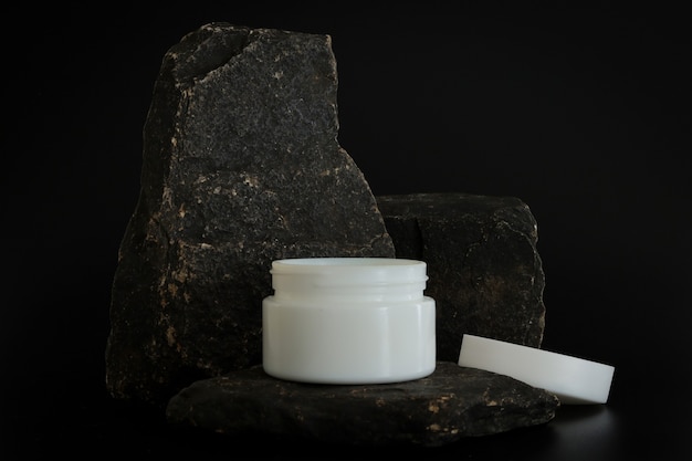 Confezione di crema cosmetica naturale senza marchio in piedi sul podio di pietra. presentazione crema sullo sfondo nero. modello. concetto di tendenza in materiali naturali. cosmetici naturali, cura della pelle.