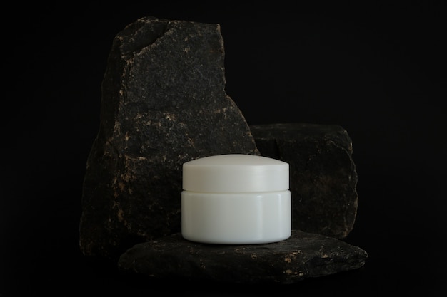 Unbranded natural cosmetic cream packaging standing on stone podium. Cream presentation on the black background. Mockup. Trending concept in natural materials. Natural cosmetic, skincare.