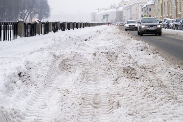 街の降雪後の大雪の吹きだまり、背景の道路上の車のある汚れた通り。冬の悪天候。