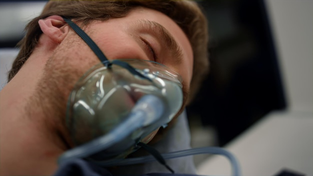 Photo unconscious man breathing in oxygen mask male patient lying on stretchers sick guy with coronavirus transferring to hospital in ambulance car closeup man wearing non invasive ventilation mask