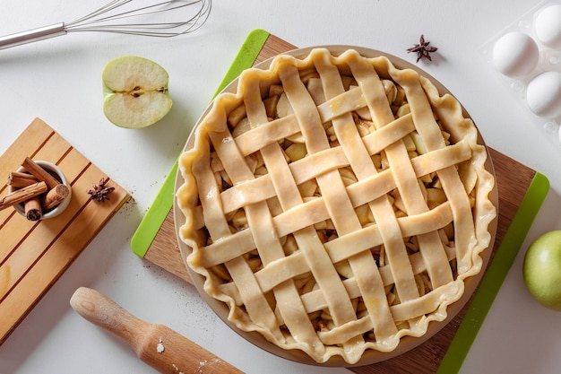 Неваренный яблочный пирог в пекарное блюдо готов к приготовлению на белом кухонном столе, окруженном ингредиентами Концепция домашней кухни Традиционный рецепт яблочного пирога на День благодарения