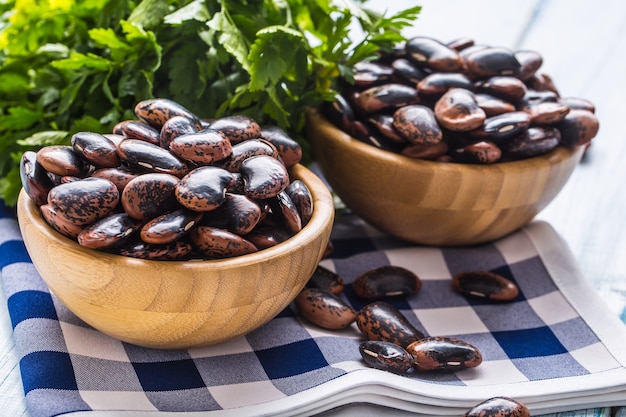 Uncooked beans in wooden bowles  with parsley herbs on kitchen table.