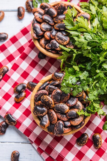 Uncooked beans in wooden bowles  with parsley herbs on kitchen table.