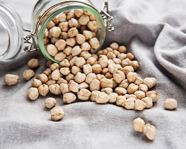 Uncooked dried chickpeas in glass jar on a grey textile background