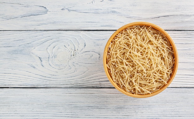 Uncooked filini pasta in wooden bowl on white wooden background with copy space