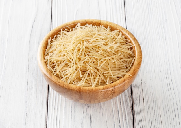 Foto pasta filini cruda in ciotola di legno su fondo di legno bianco