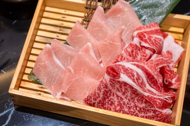 Uncooked fresh sliced pork and beef put in a wooden square box that preparing for Shabu