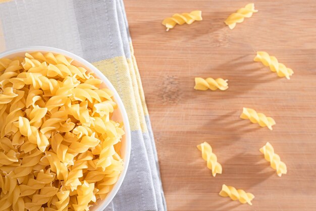 Uncooked Fusilli Pasta in White Bowl on Wooden Board