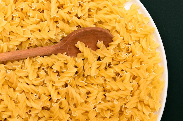 Uncooked fusilli pasta with wooden spoon