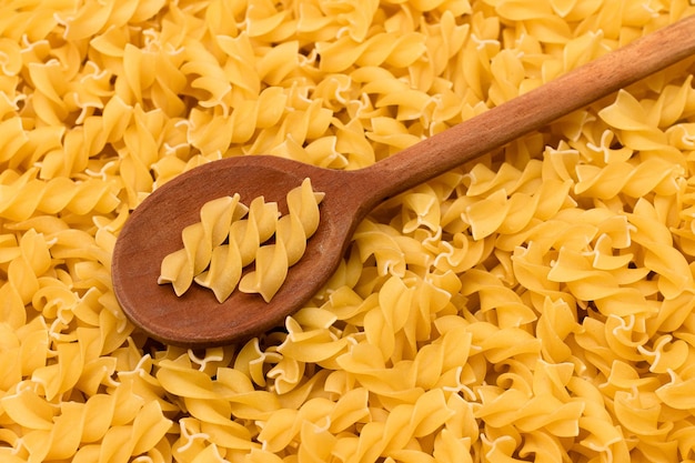 Uncooked fusilli pasta with wooden spoon