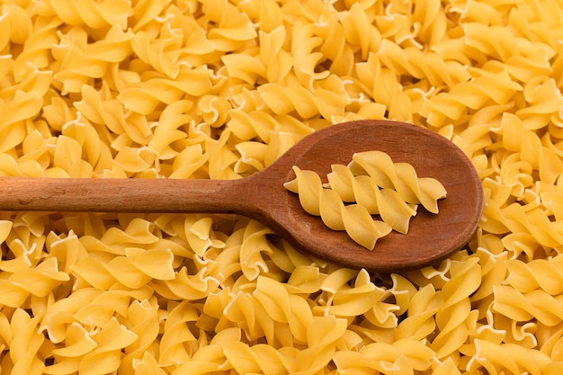 Uncooked fusilli pasta with wooden spoon