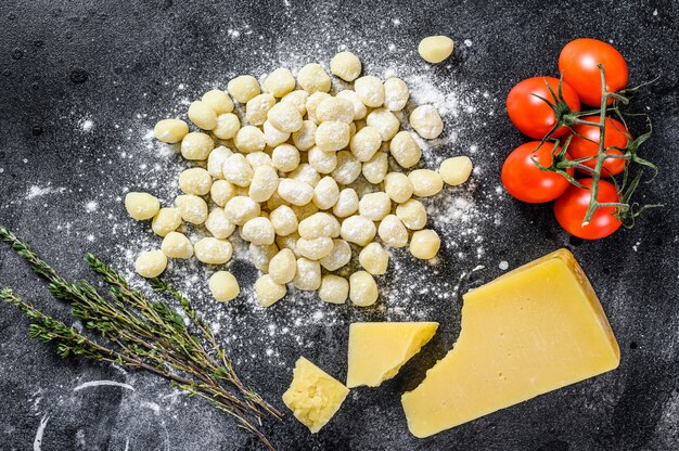 Uncooked homemade gnocchi on black cutting board. Black background. Top view