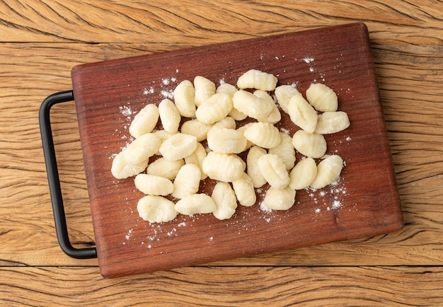 Uncooked italian pasta gnocchi on a board over wooden table.