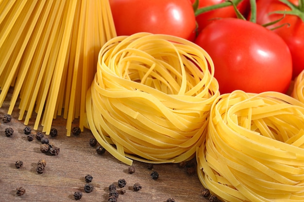 Uncooked Italian pasta, ripe tomatoes branch and black pepper on a wooden background