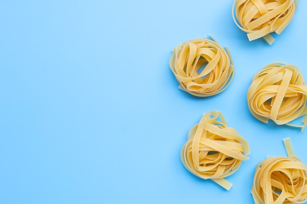 Nido di tagliatelle di pasta italiana non cotte sulla superficie blu