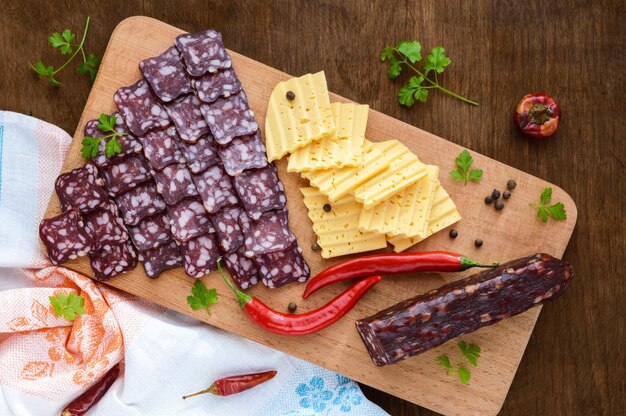 Uncooked jerked sausage cheese cutting slices on a cutting board on a dark wooden background