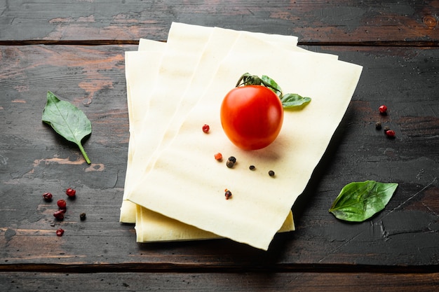 Uncooked lasagna sheets with seasoning and herb on old wooden table