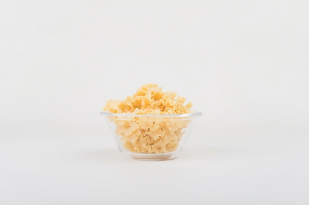 Uncooked mafalde corte pasta in a clear glass bowl with white background