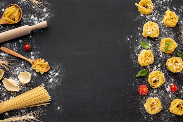 Uncooked pasta assortment with flour on black background