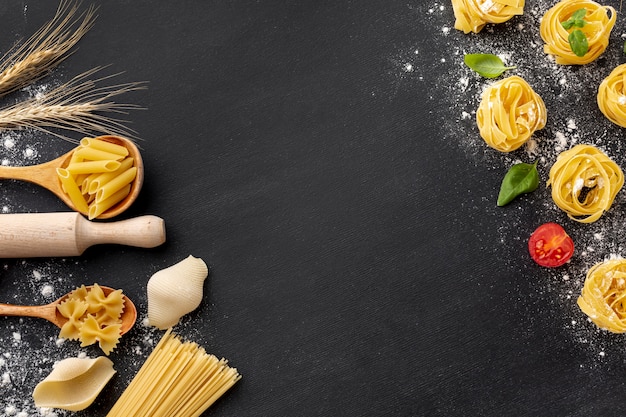 Photo uncooked pasta assortment with flour and rolling pin on black background